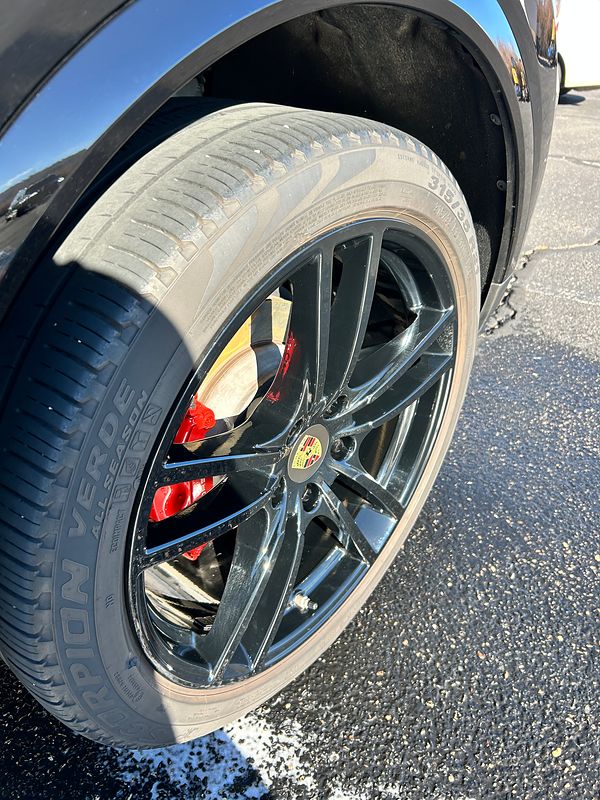 After: the same Porsche wheel, clean gloss black, with the tire dressed
