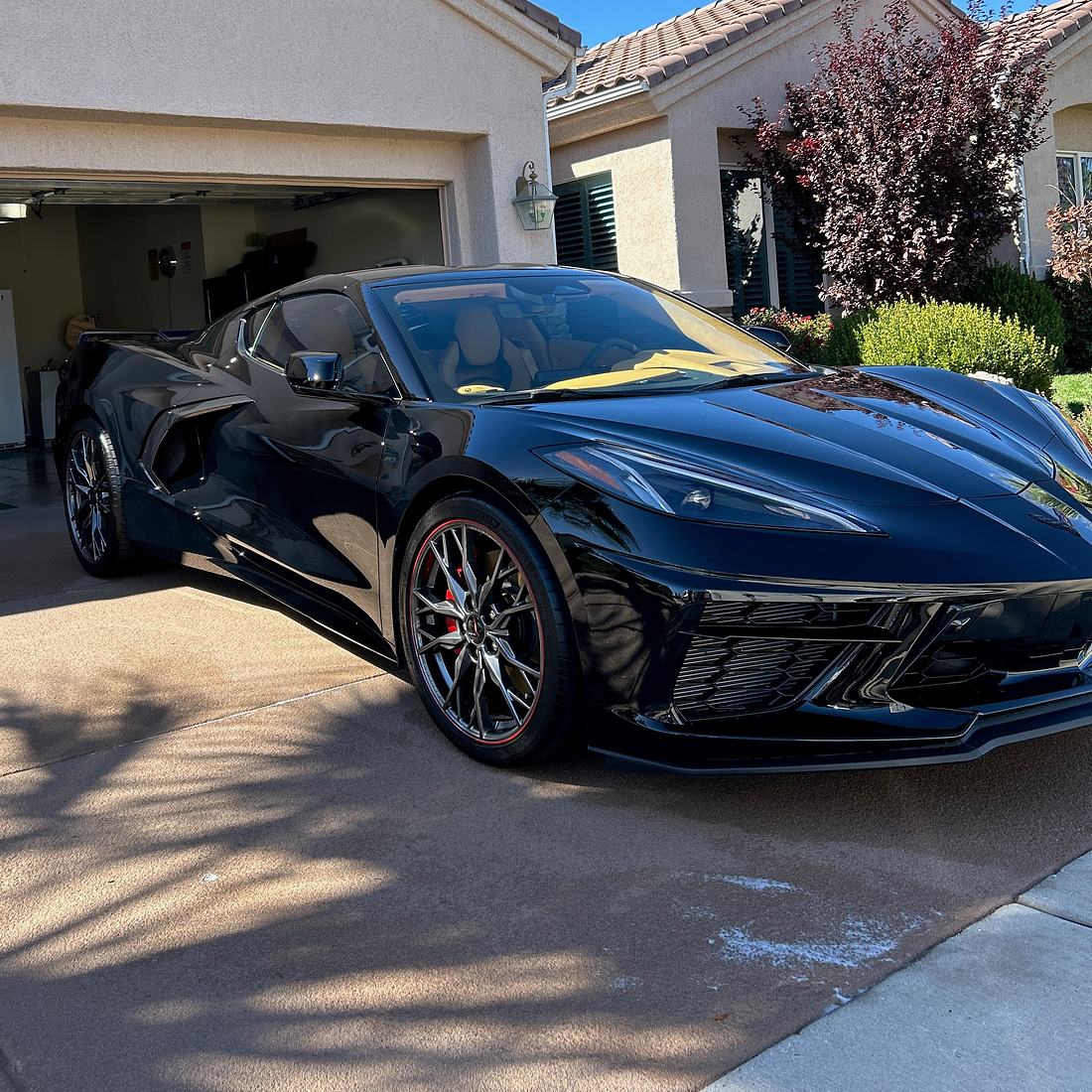 A black C8 Corvette, just detailed, on a driveway in front of an open garage