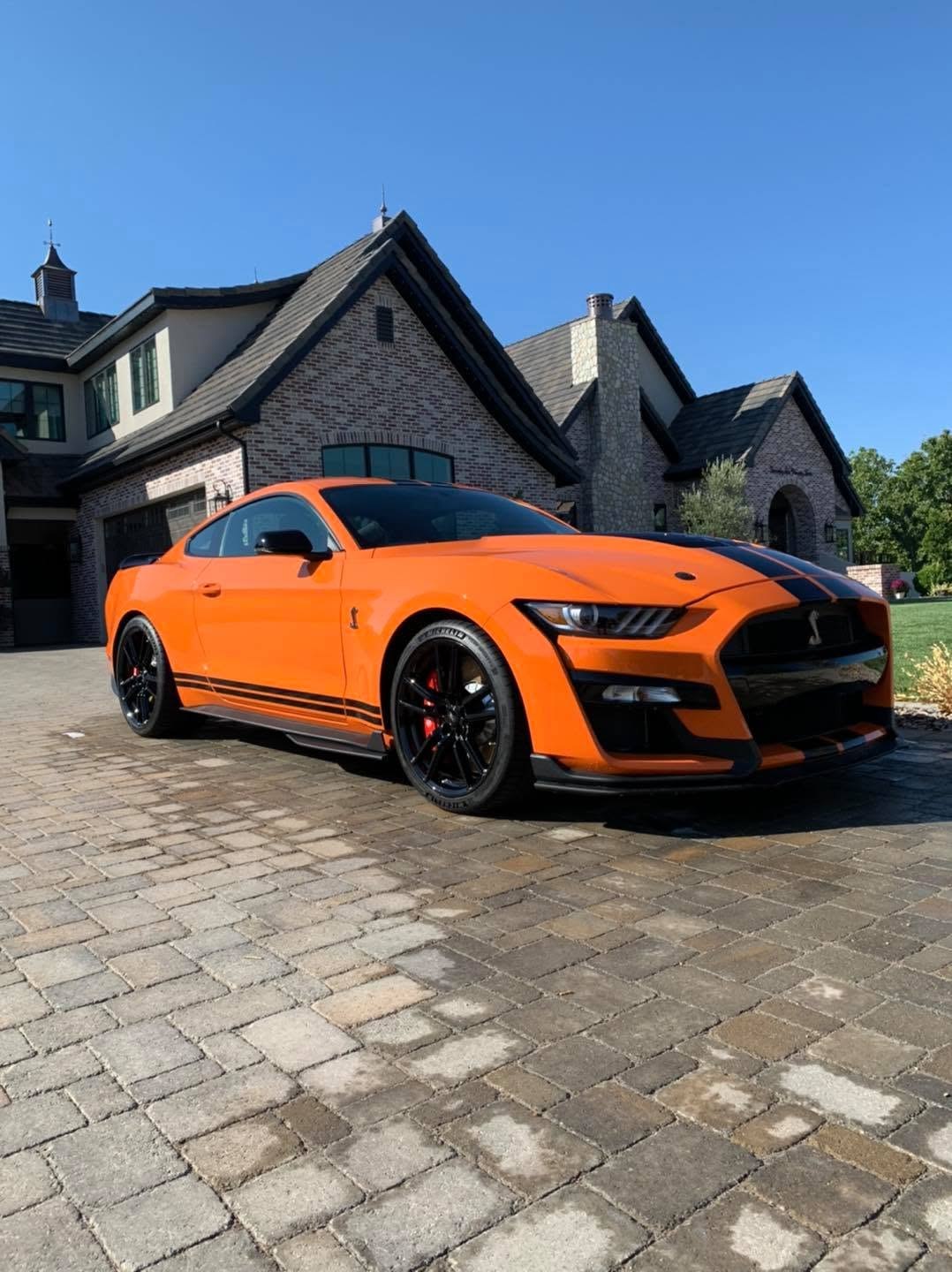 An orange Shelby GT500 with black stripes, polished, on a paver driveway