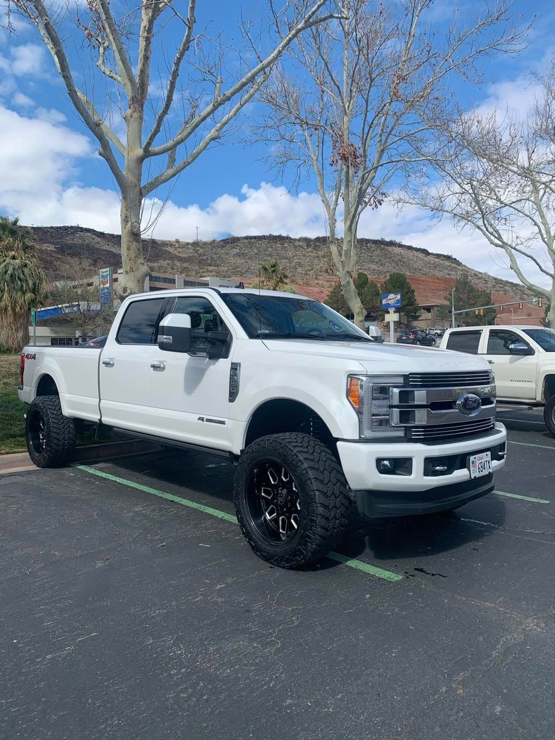 A clean white Ford Super Duty pickup on black wheels, parked with red hills behind